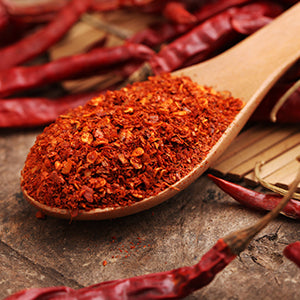 Ground cayenne pepper in a spoon with cayenne peppers in the background.