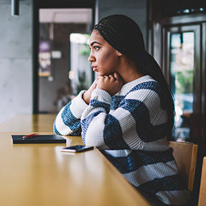 A woman in a striped sweater with hands cupped to her chin in an indoor setting while looking out.