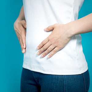 A woman with her hands to her abdominal area in a blue background.