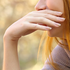 A woman is covering her mouth. Allergies and diabetes can cause bad breath.