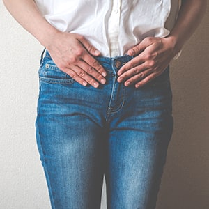 A person is holding their abdominal area. Flat incontinence can occur at any time.