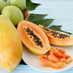 Papaya fruit cut in half with smaller pieces on a plate with green leaves in the background.