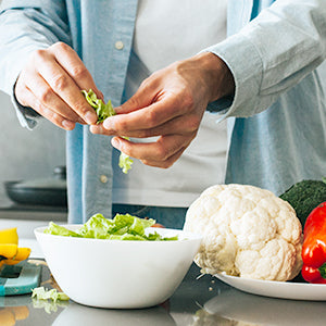 A person handling lettuce with bowls of vegetables over a kitchen counter.