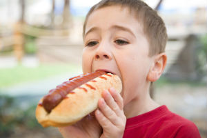 Picture of a child eating a hot dog depicting the risk of developing cancer by eating processed foods such as processed hot dog meat.