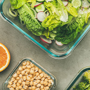 A meal prep which includes chickpeas, a salad, raw vegetables, and a juice.