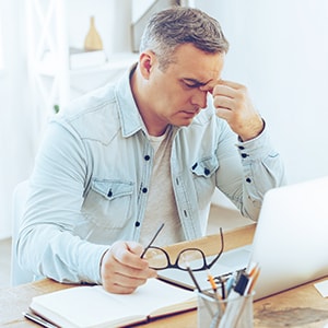 A tired older man sitting in front of laptop in office after a hard working day.