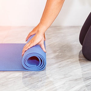 A woman folding up her yoga mat. Pilates with yoga and strength training can lead long-term, natural, weight loss.