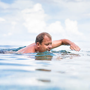 A man swimming in blue water on a sunny day.